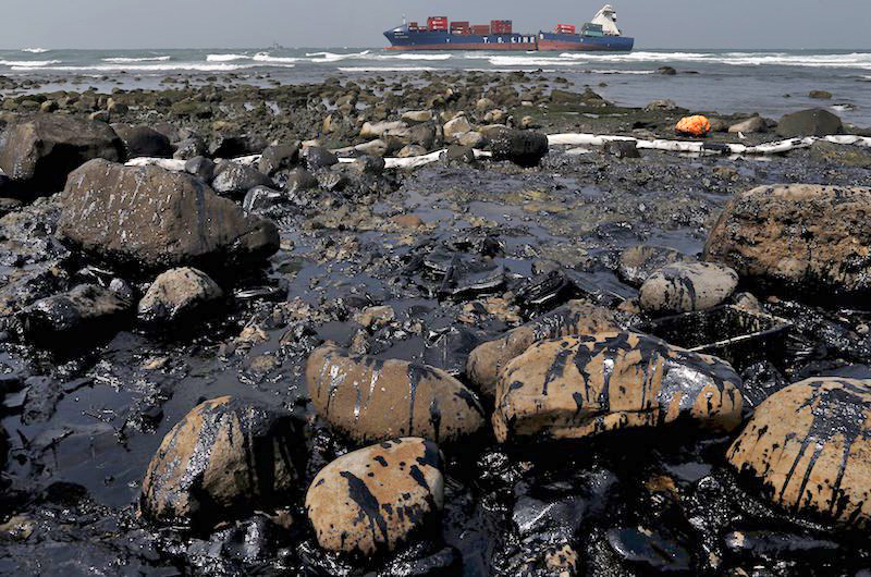 Rocks covered with oil that leaked from a cargo ship (background) owned by TS Lines Co are seen off the shores of New Taipei City, Taiwan, March 26, 2016. The oil spilled from the ship has contaminated 2 kilometer (1.24 miles) of water, according to local media. REUTERS/Tyrone Siu